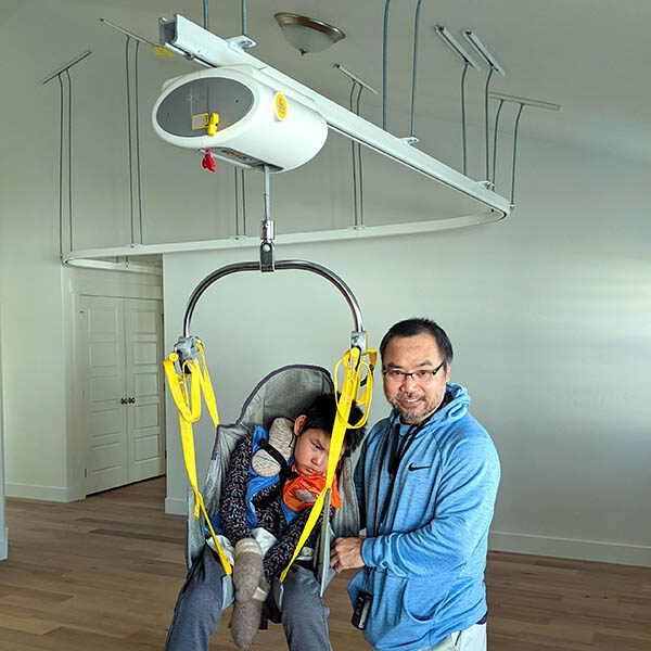 man helps his son in overhead ceiling lift system safely transfer around home