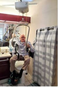 older adult uses ceiling lift body support to safely use toilet in bathroom