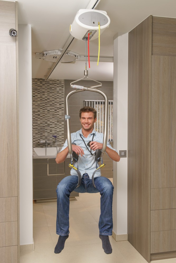 man using body support system of SureHands ceiling lift from Lifeway Mobility to transfer from one room to another